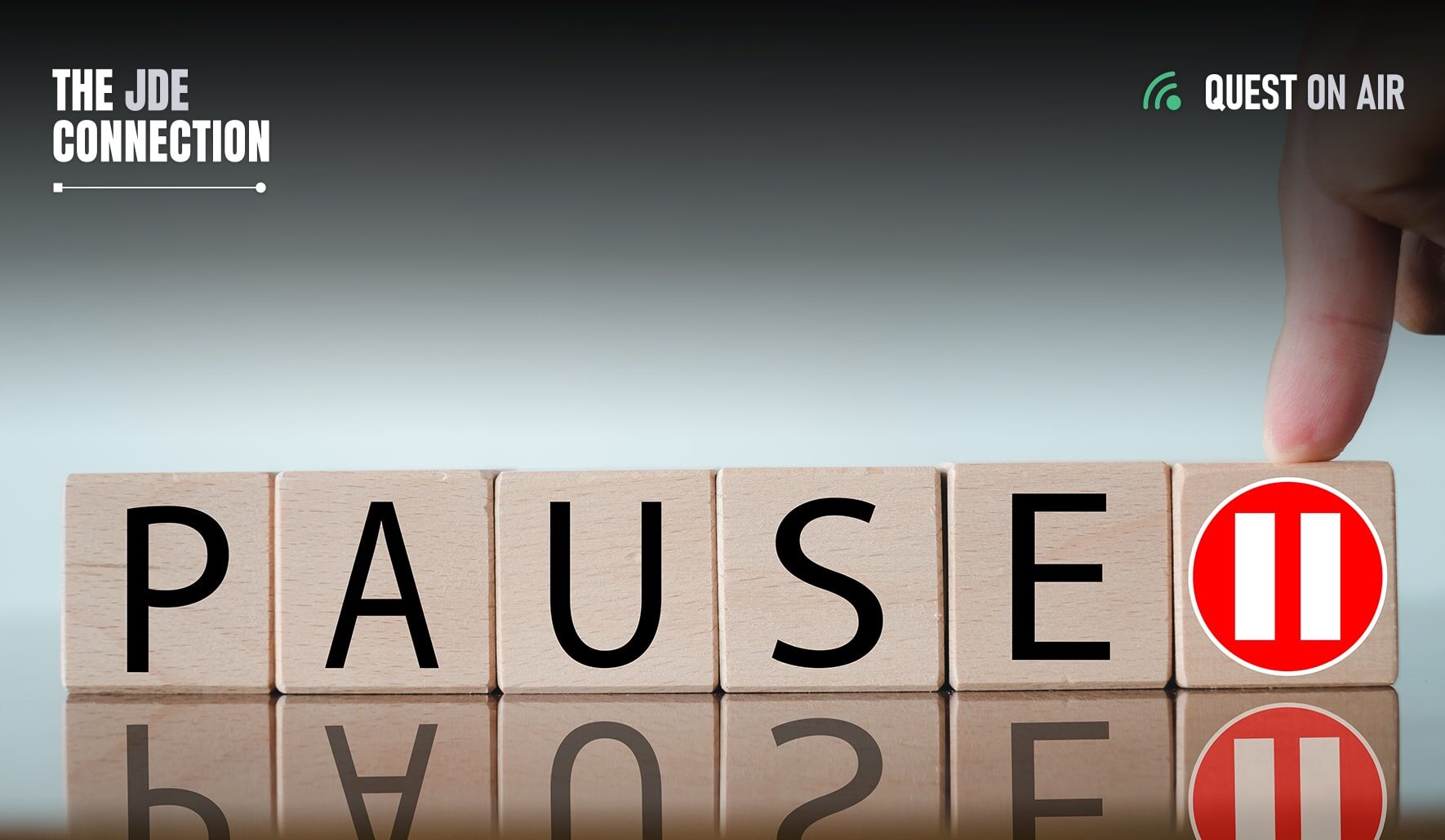 The JDE Connection logo in upper left with Quest on Air logo in upper right over wooden blocks that spell out PAUSE with an orange pause icon being pressed by a finger on the rightmost block